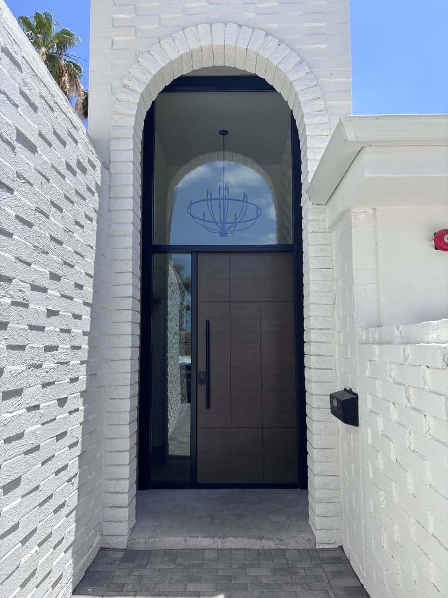 Custom pivot entry door with full-height glass in a white brick archway